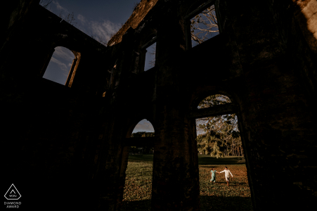 Fazenda Flor do Vale couple engagement portraits with a couple strolling on lawn being framed by a window of a dilapidated office