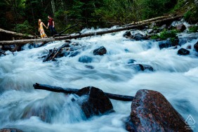 Het verloofde stel steekt de woeste rivier over terwijl ze balanceren op een boomstam tijdens portretten in Frisco, CO