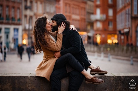 Portrait of a Toulouse couple kissing cross legs sitting on a wall