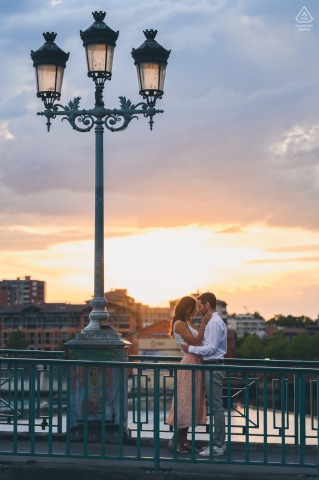 A Toulouse couple on a bridge with sunset background and a tall lamp post