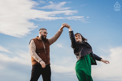 During their engagement portrait session in Basque Country France, a dancing couple was captured against a cloudy blue sky with minimalistic framing.