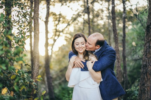 Durante su sesión de compromiso al final de la tarde en Seaside, Florida, el hombre abraza amorosamente a la mujer desde atrás en el entorno del bosque.