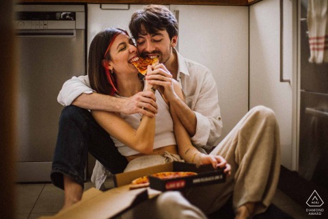 The engaged couple in İstanbul Kadıköy share a joyful pizza feast together, seated on the kitchen floor, brimming with smiles as they prepare for their upcoming wedding.