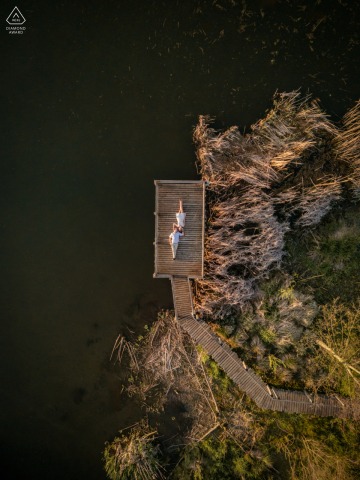 At Biebersee in Cham, a drone shot captures the couple laying on their backs on a wood deck by the water, capturing the love and anticipation of their upcoming marriage.