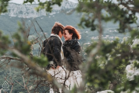 Together, on the breathtaking cliff at Mont Coudon in Var, PACA, France, the couple embraces, kisses, and is surrounded by lush foliage - a picturesque scene capturing their love before their wedding.