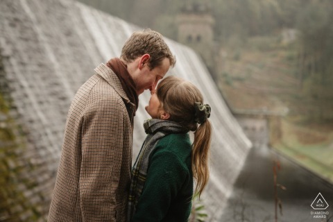 At Derwent Reservoir, Peak District, UK, the soon-to-be-wed couple embrace lovingly, with the iconic Dambusters practicing dam as a backdrop for their engagement portrait.