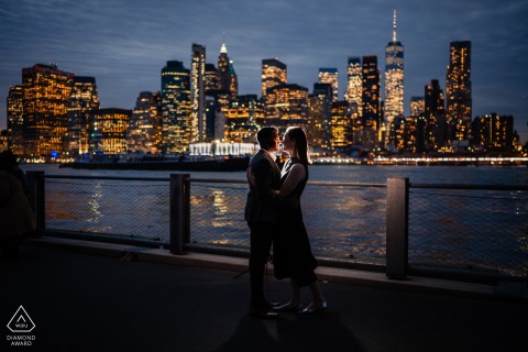 At Dumbo, NY, a couple dressed in formal clothing face each other with the NYC skyline as their backdrop, illuminated by a subtle strobe light from behind, capturing their love before they say 'I do.'