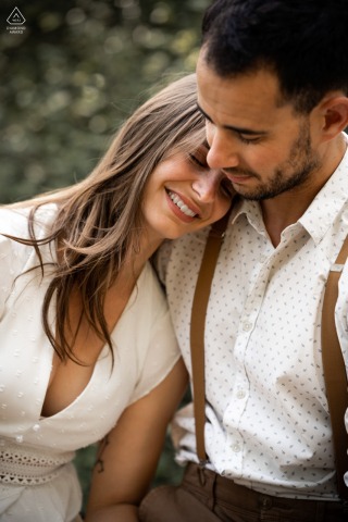 During their engagement portrait session in Vals-les-Bains, France, the couple embraced in a warm hug, with her leaning into him and resting her head on his shoulder, both sharing joyful smiles that spoke of their deep love for each other.
