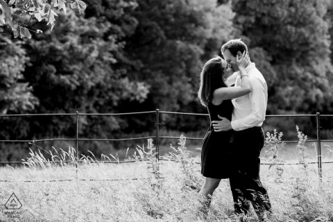 In Wellington, Somerset, teilt ein verliebtes Paar einen süßen Kuss auf einer sonnigen Wiese neben einem Drahtzaun, wunderschön in Schwarzweiß festgehalten.