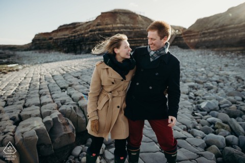 Am Porlock Beach in Nord-Devon wiegt sich das Paar gemeinsam und lacht, während es während seiner Verlobungsporträtsitzung an der felsigen Küste entlang spaziert.
