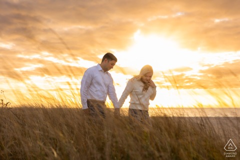 At Dowsers' Beach in Osterville, Massachusetts, a couple walks together in a field of tall grass, basking in the warm light of the setting sun, encapsulating their love.