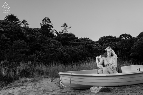 In Bourne, MA, a couple about to wed share a special photo shoot, filled with smiles and love, on a peaceful beached boat by the quiet dunes.