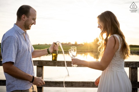 In Cham, Switzerland, the couple poses together for their engagement photos, with the groom-to-be holding a popping champagne bottle while the bride-to-be holds two empty glasses.