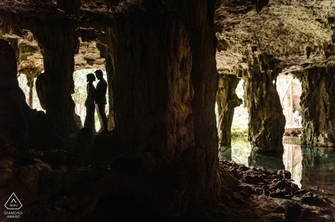 Au complexe cénote Dos Ojos à Tulum, au Mexique, un couple se préparant au mariage pose pour des photos dans une grotte, la lumière créant une silhouette d'eux dans l'embrasure d'une porte.