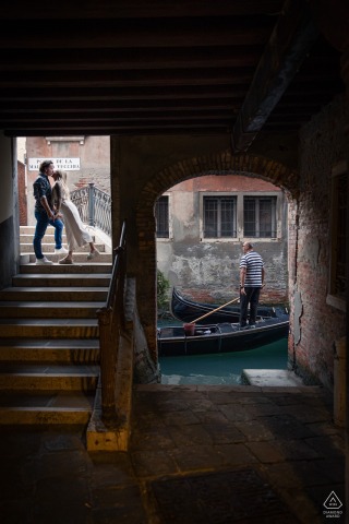 In Venice, Italy, a loving couple getting married poses for pictures by kissing off the beaten path while a gondola operator glides by in the background.