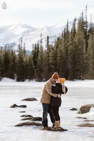 In Arapaho National Forest, Colorado, a couple poses for pictures on a frozen alpine lake with the sun setting behind them, creating a beautiful backdrop for their engagement photos.