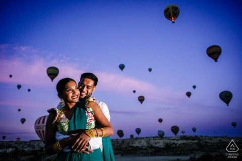 During their pre-wedding photo session in Cappadocia, Turkey, the couple embraced, smiled, and were lit up by the photographer against a backdrop of a blue and purple sky filled with hot air balloons.