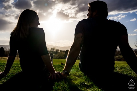 In Arvada, CO, USA, the soon-to-be-married couple sat on the grass in the park at sunset, gazing at each other with their silhouettes captured in a romantic photo.