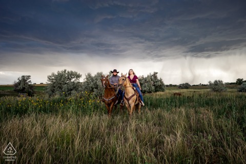 In Colorado, near Johnstown, a couple on horses posed on a stormy day, riding through the grass fields, creating a symmetrical and beautiful portrait before their wedding.