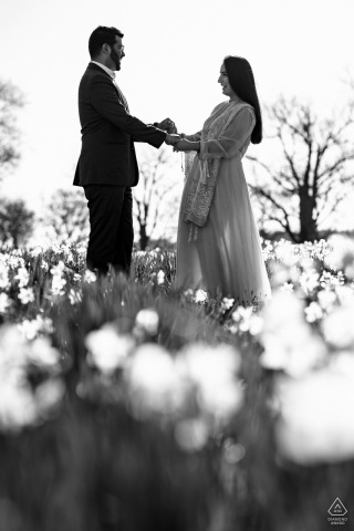 At Harkness Park in Waterford, CT USA, a couple stands in a daffodil field, holding hands with lots of plants all around them. The photo is in black and white.