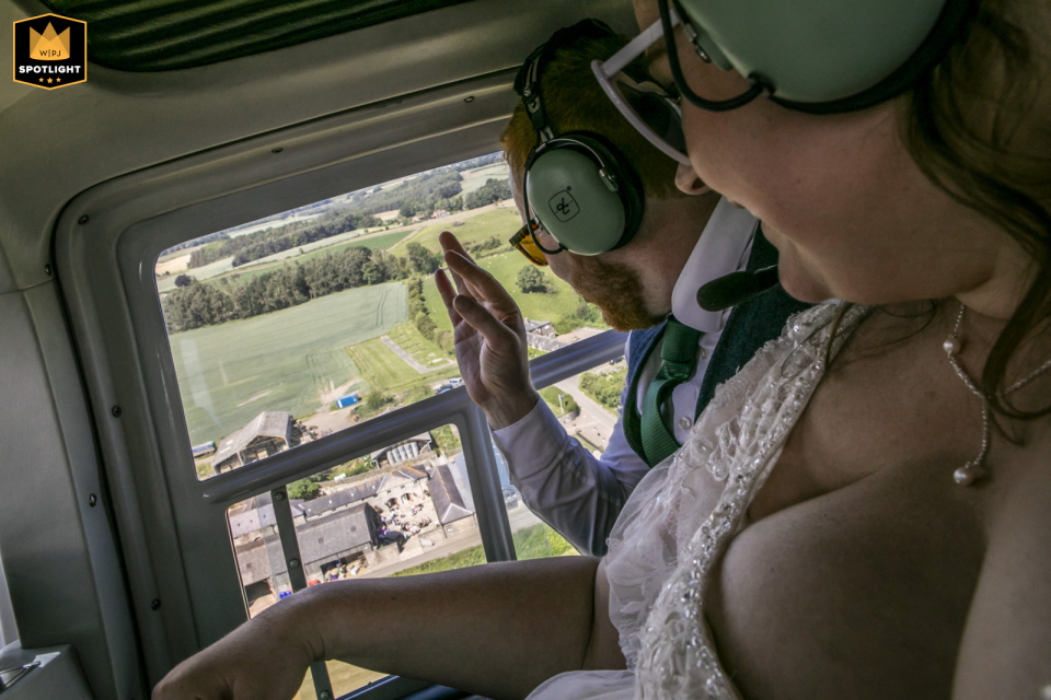 Photographer captures wedding couple waving to guests from a helicopter at Doxford Barns, Northumberland, UK.